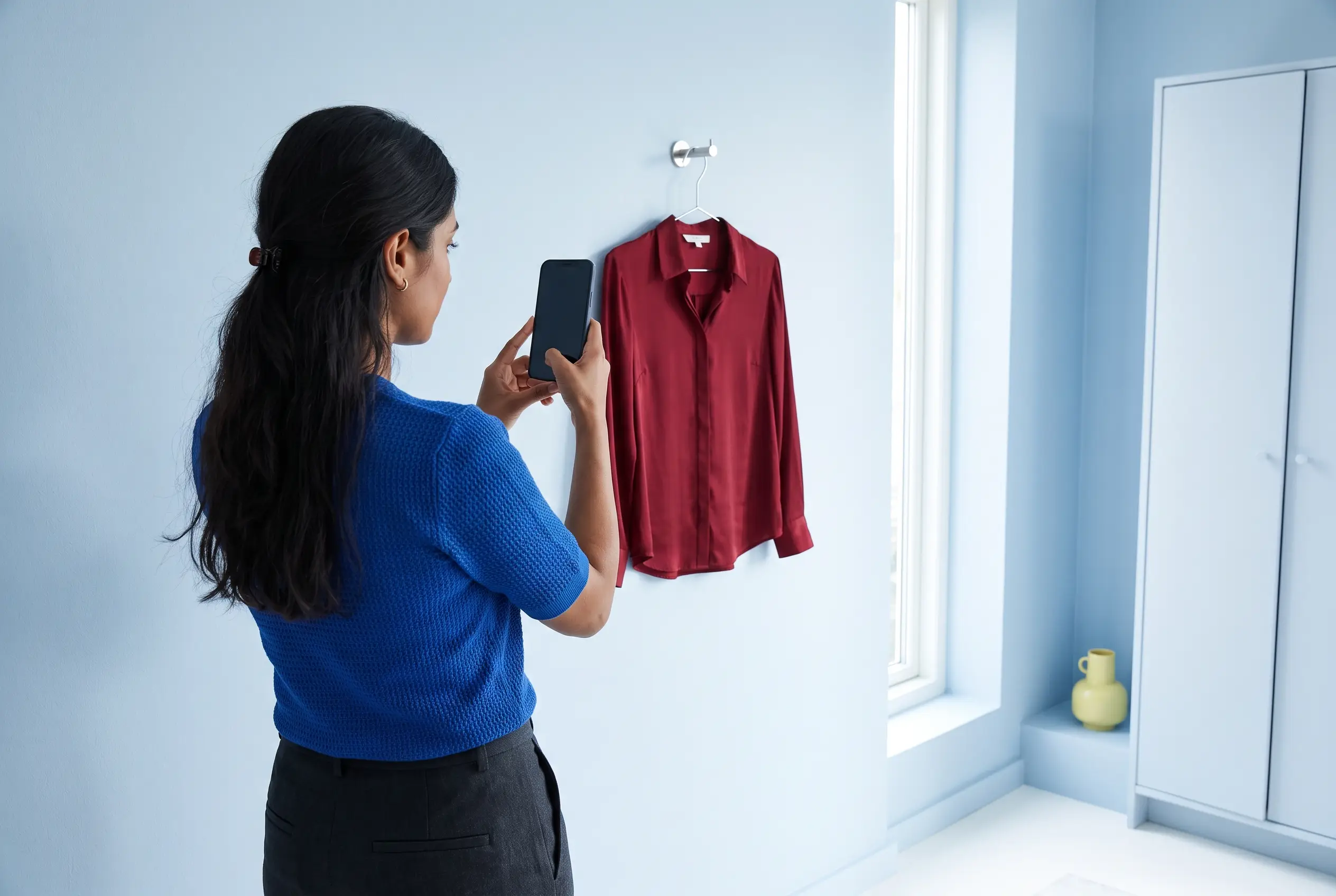 A woman photographing a blouse hanging in clear daylight